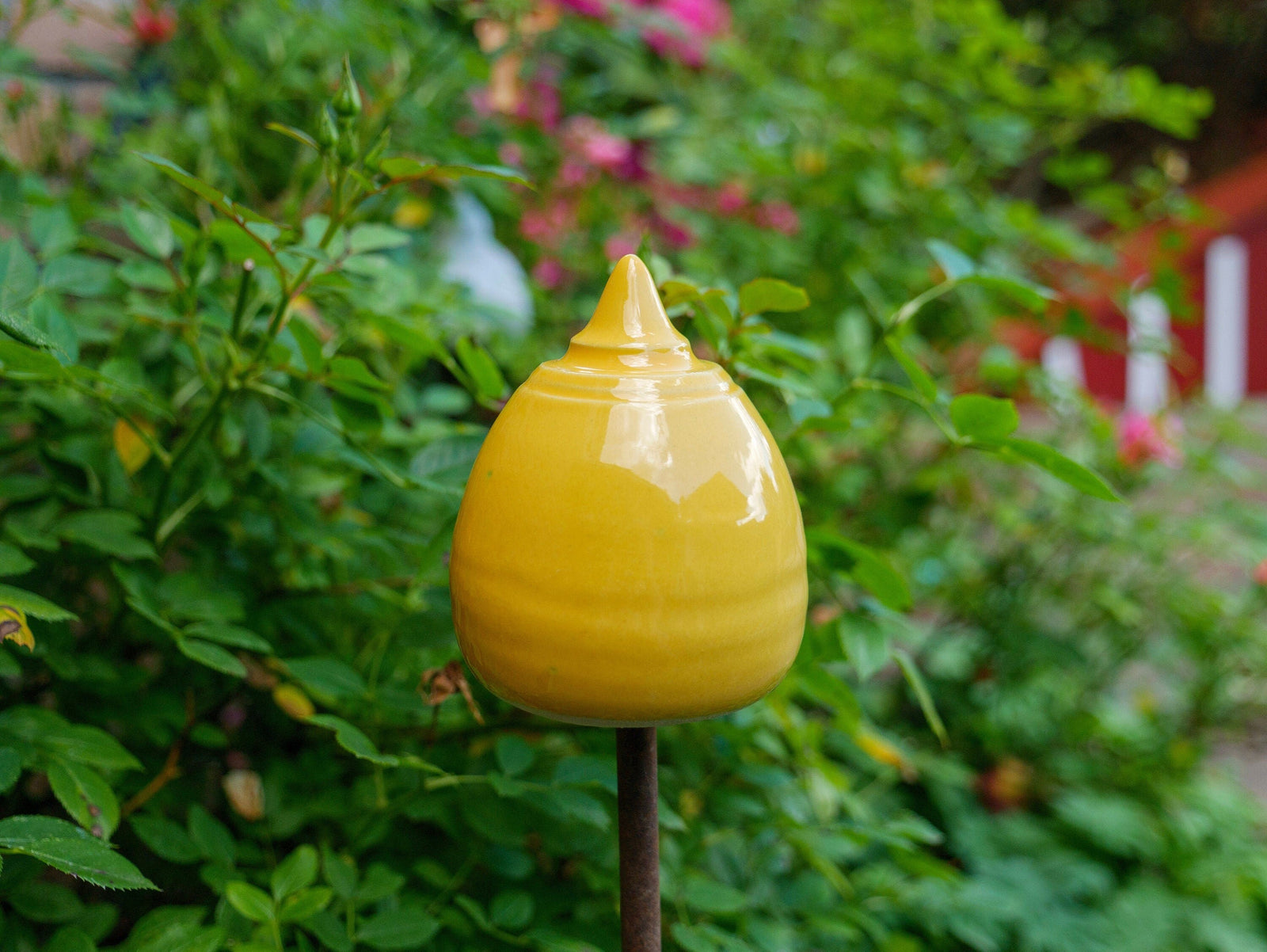 Gelbe Keramik-Gartendekoration in gestufter, glockenähnlicher Form zwischen grünen Pflanzen