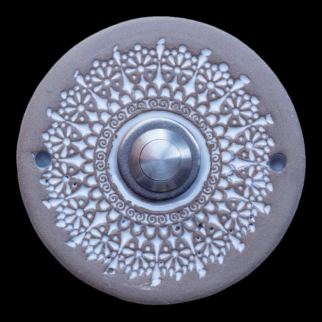 Runde Keramikklingel mit filigranem, spitzenartigem Blumenmuster in Weiß und zentralem silbernen Knopf