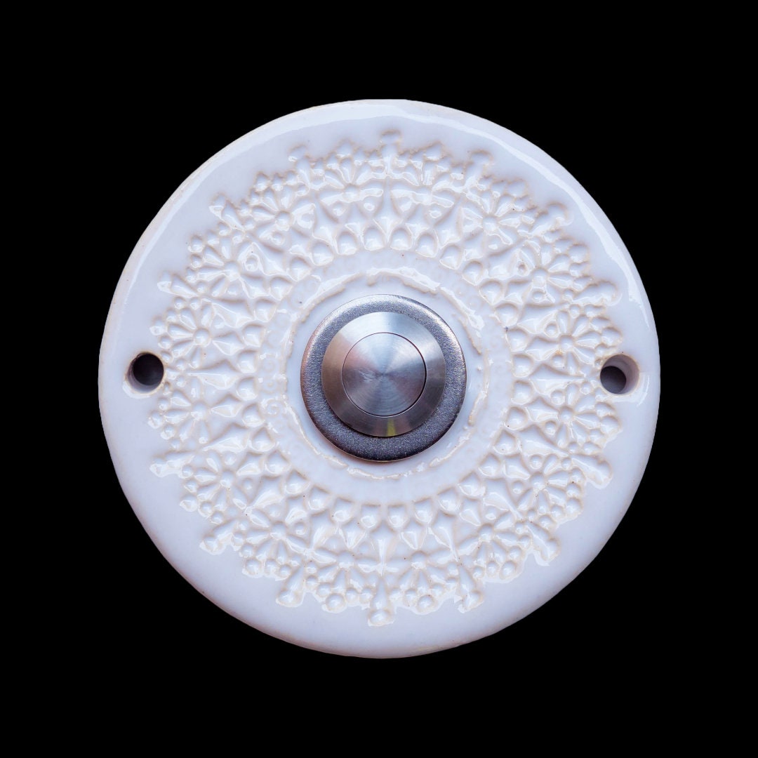 Runde Keramikklingel mit filigranem, spitzenartigem Blumenmuster in Weiß und zentralem silbernen Knopf