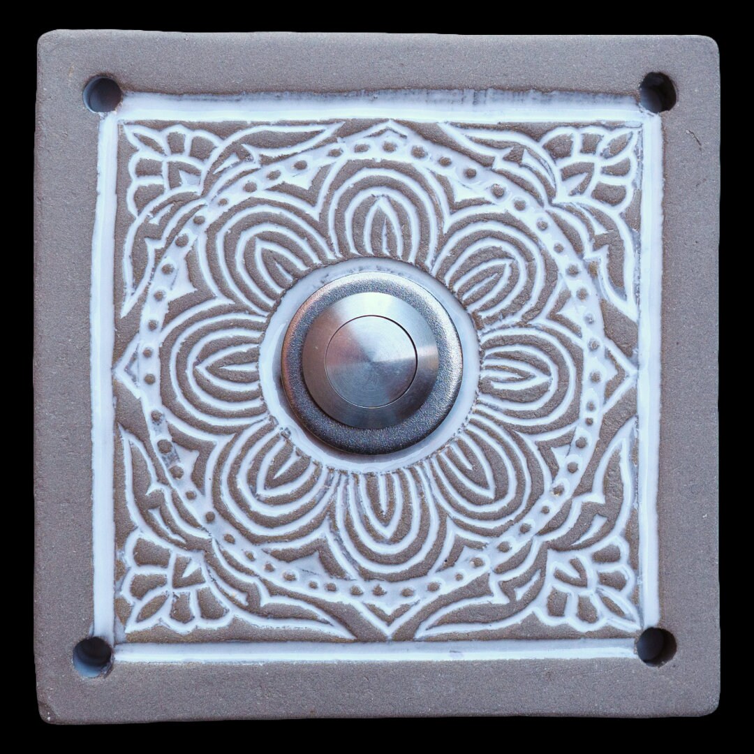 Quadratische Keramik-Türklingel mit kunstvollem Mandala-Muster in weißem Relief und silbernem Knopf in der Mitte