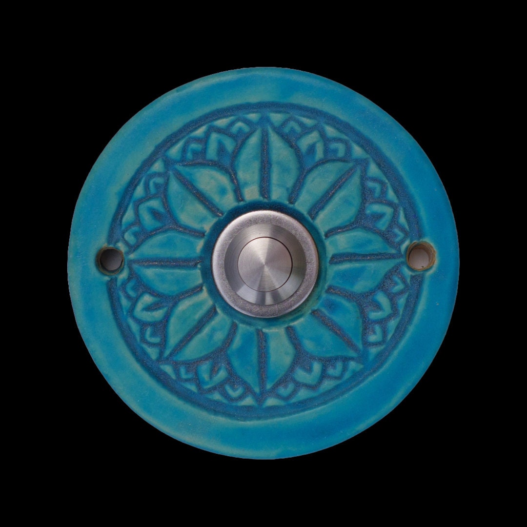 Runde dekorative Klingel mit geprägtem Mandala-Blumenmuster auf leuchtend blauer Platte und silbernem Druckknopf in der Mitte.