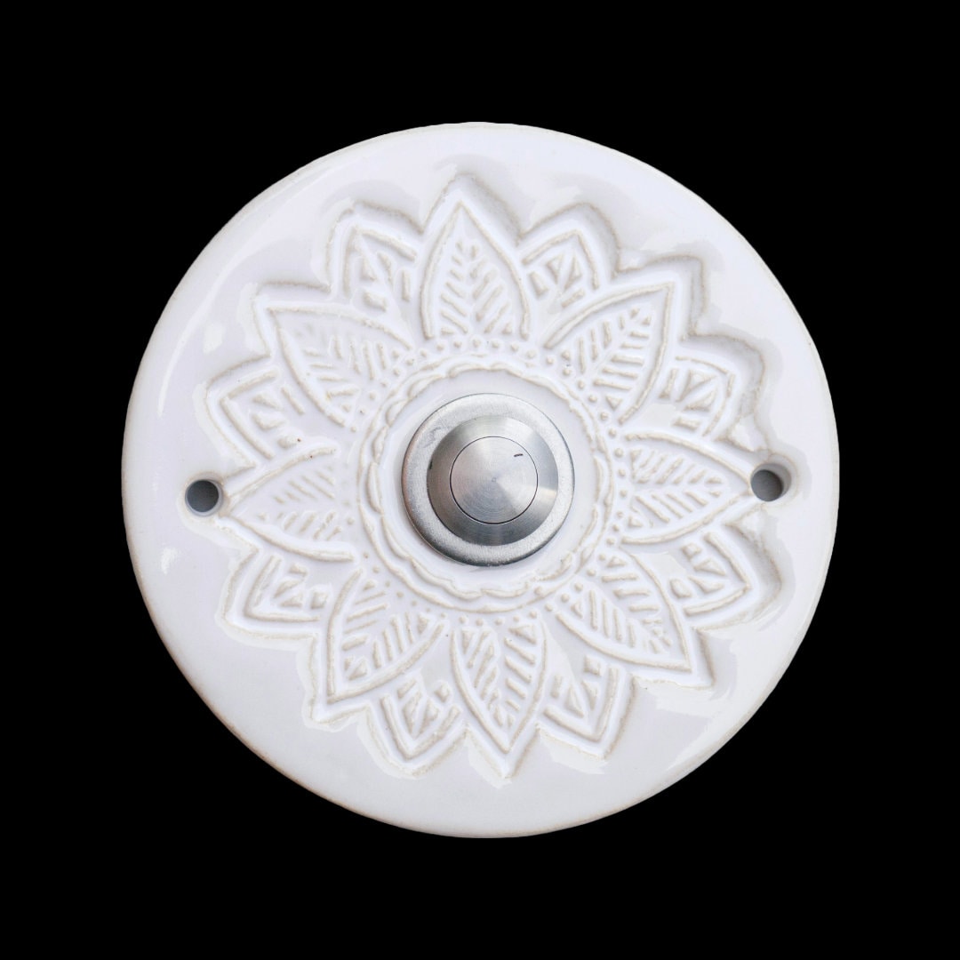 Runde dekorative Klingel mit geprägtem Mandala-Blumenmuster auf glänzender weißer Platte und silbernem Druckknopf in der Mitte