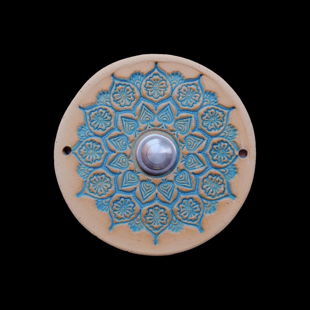 Runde Keramikklingel mit filigranem, spitzenartigem Blumenmuster in Weiß und zentralem silbernen Knopf