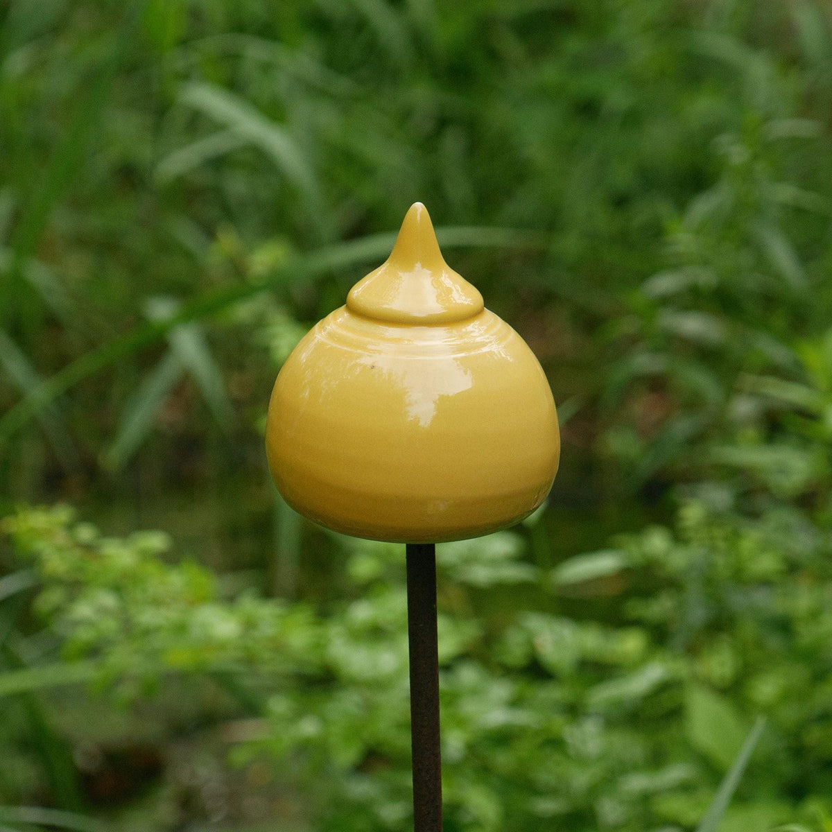 Handgefertigte Keramik-Gartenstele in glänzendem Senfgelb mit abgerundeter Kegelform, aufgestellt zwischen blühenden rosa Rosen
