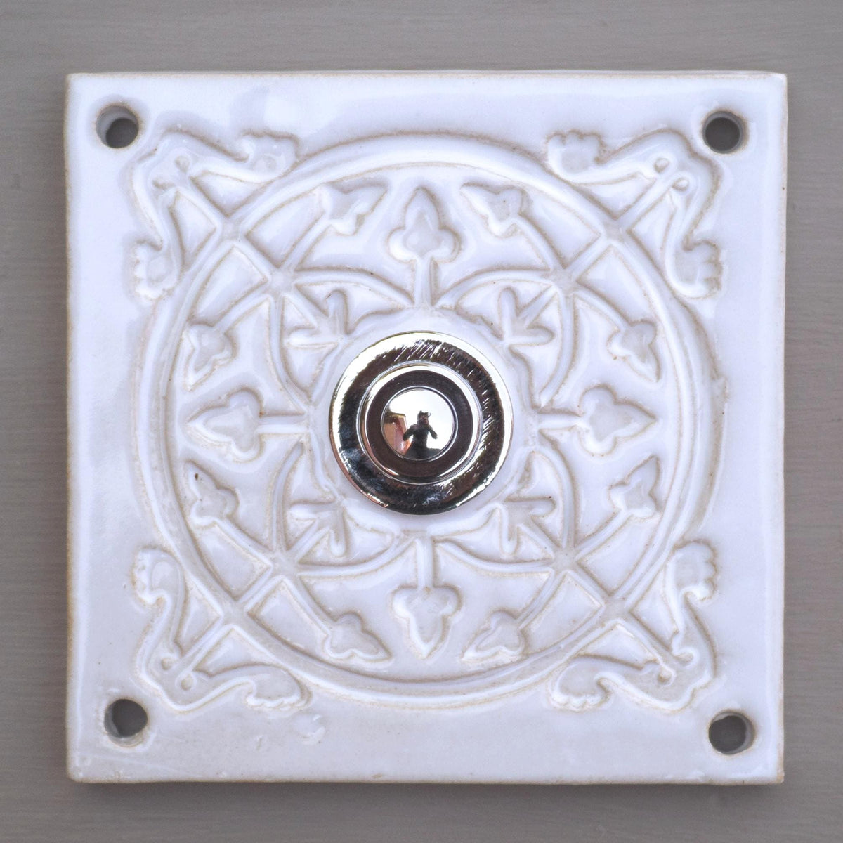 Quadratische dekorative Keramikklingel mit geprägtem floralen Mandala-Muster in Reinweiß und silbernem Druckknopf in der Mitte