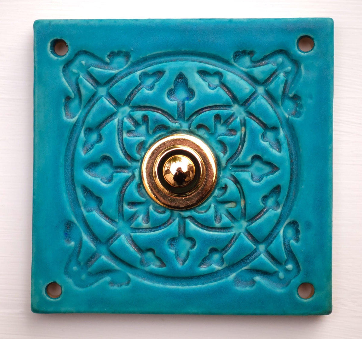 Quadratische Keramikklingel in Türkisblau mit geprägtem Mandala-Muster und goldenem Druckknopf in der Mitte