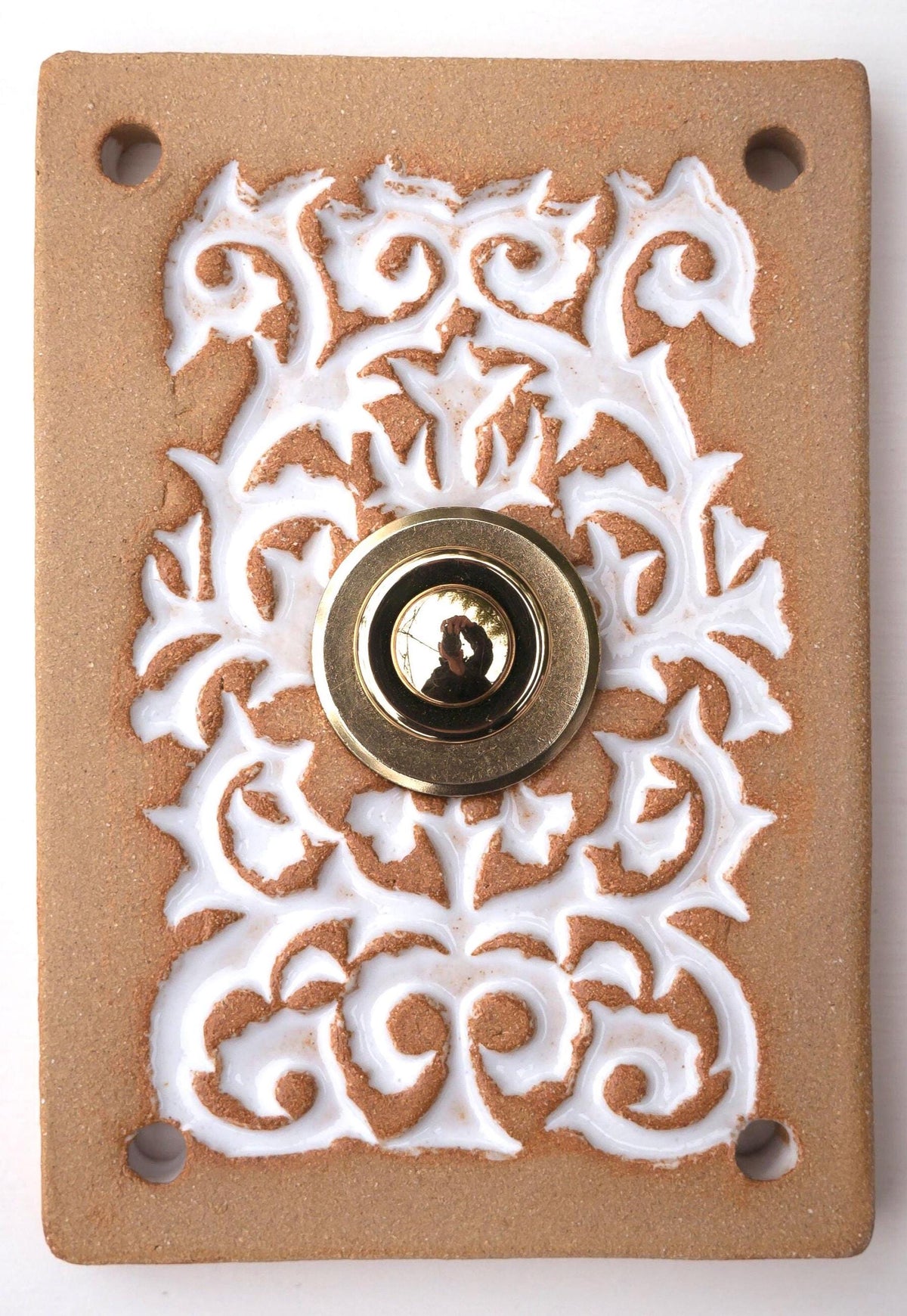Rechteckige Keramikklingel in Goldbraun-Weiß mit kunstvollem Reliefmuster und zentralem Messing-Druckknopf