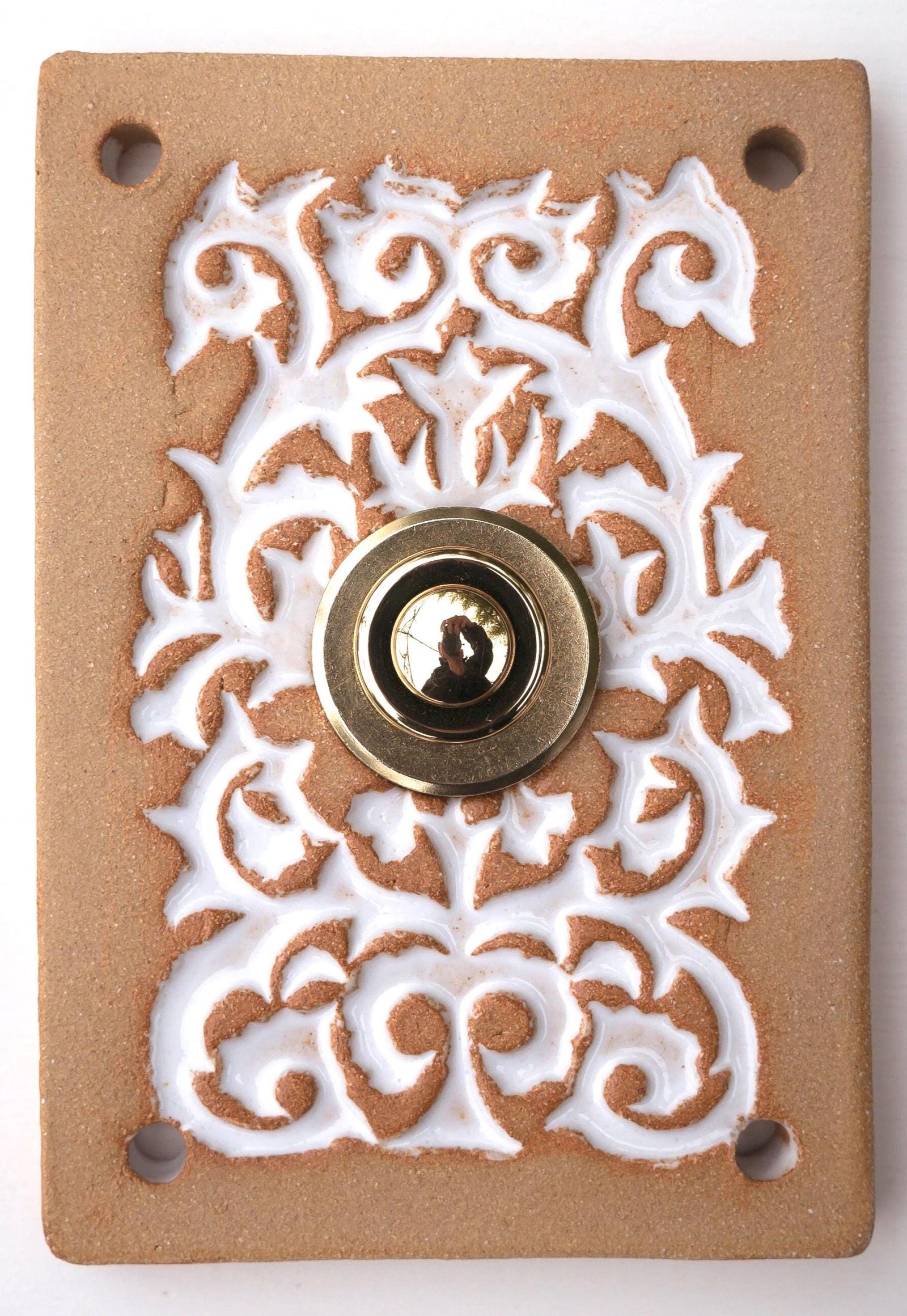 Rechteckige Keramikklingel in Goldbraun-Weiß mit kunstvollem Reliefmuster und zentralem Messing-Druckknopf