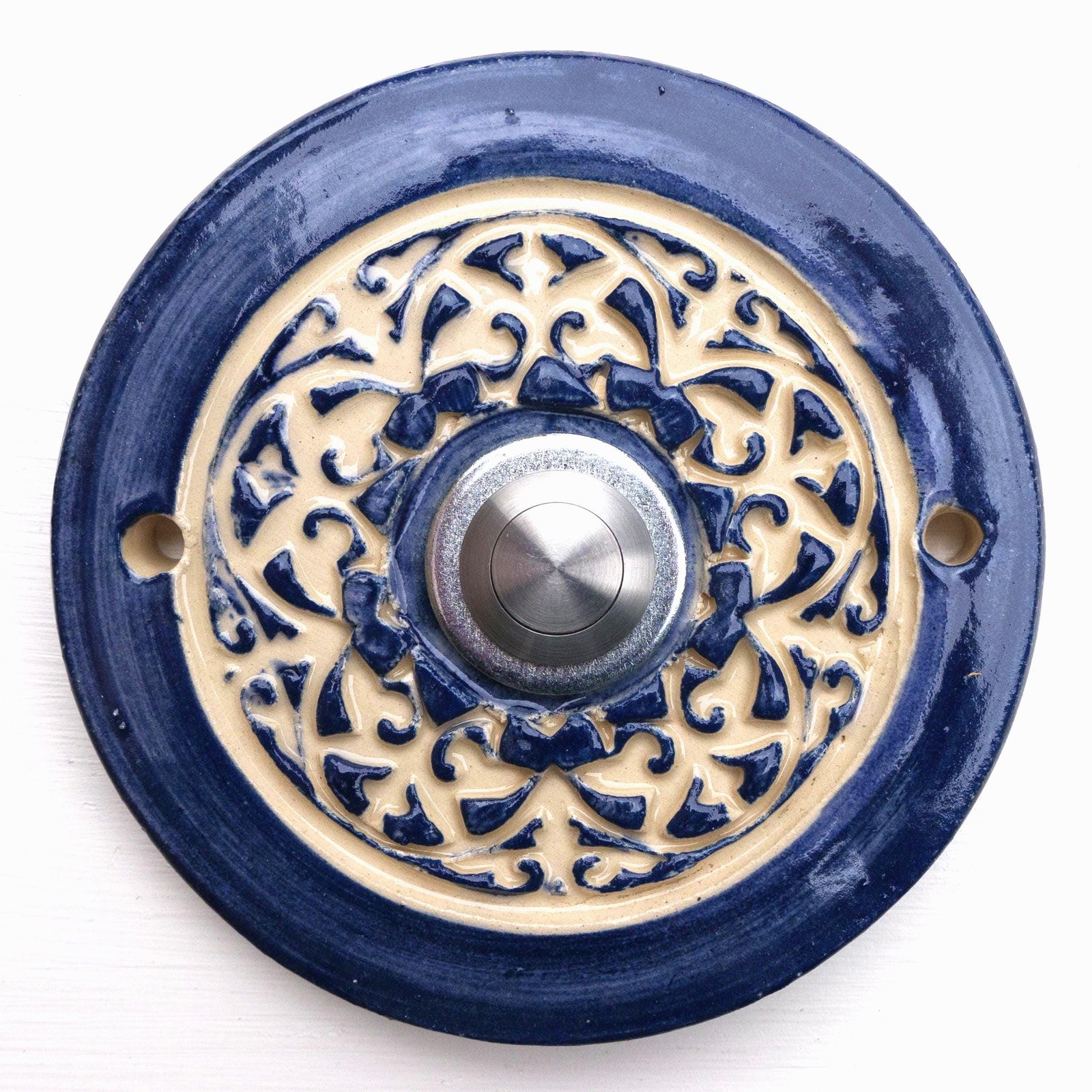 Handgefertigte runde Keramiktürklingel in kräftigem Blau mit kunstvollem cremefarbenem Reliefmuster. Ein zeitloses Stück, das traditionelle Handwerkskunst mit einem modernen Edelstahlknopf verbindet.