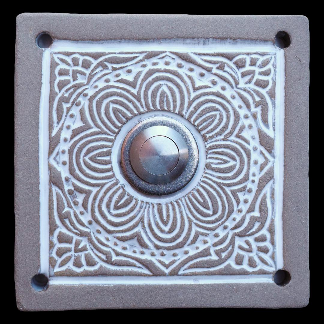 Handgefertigte Keramiktürklingel in natürlichem Beige mit filigranem weißem Mandala-Muster. Der silberne Knopf harmoniert perfekt mit dem kunstvollen Design und macht diese Türklingel zu einem stilvollen Blickfang für Ihren Eingangsbereich.