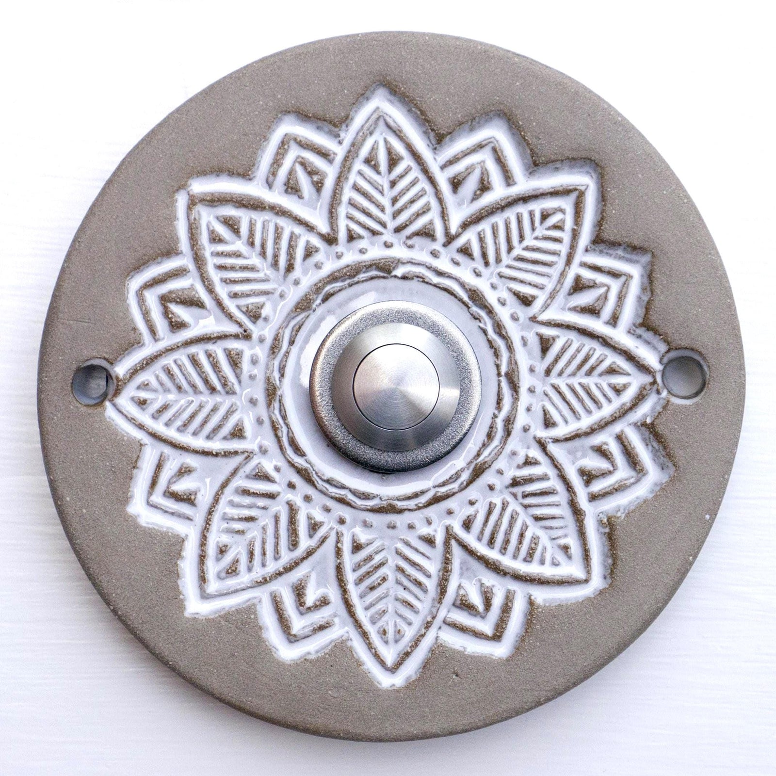 Runde dekorative Klingel mit geprägtem weißem Mandala-Blumenmuster auf grauer Platte und silbernem Druckknopf in der Mitte