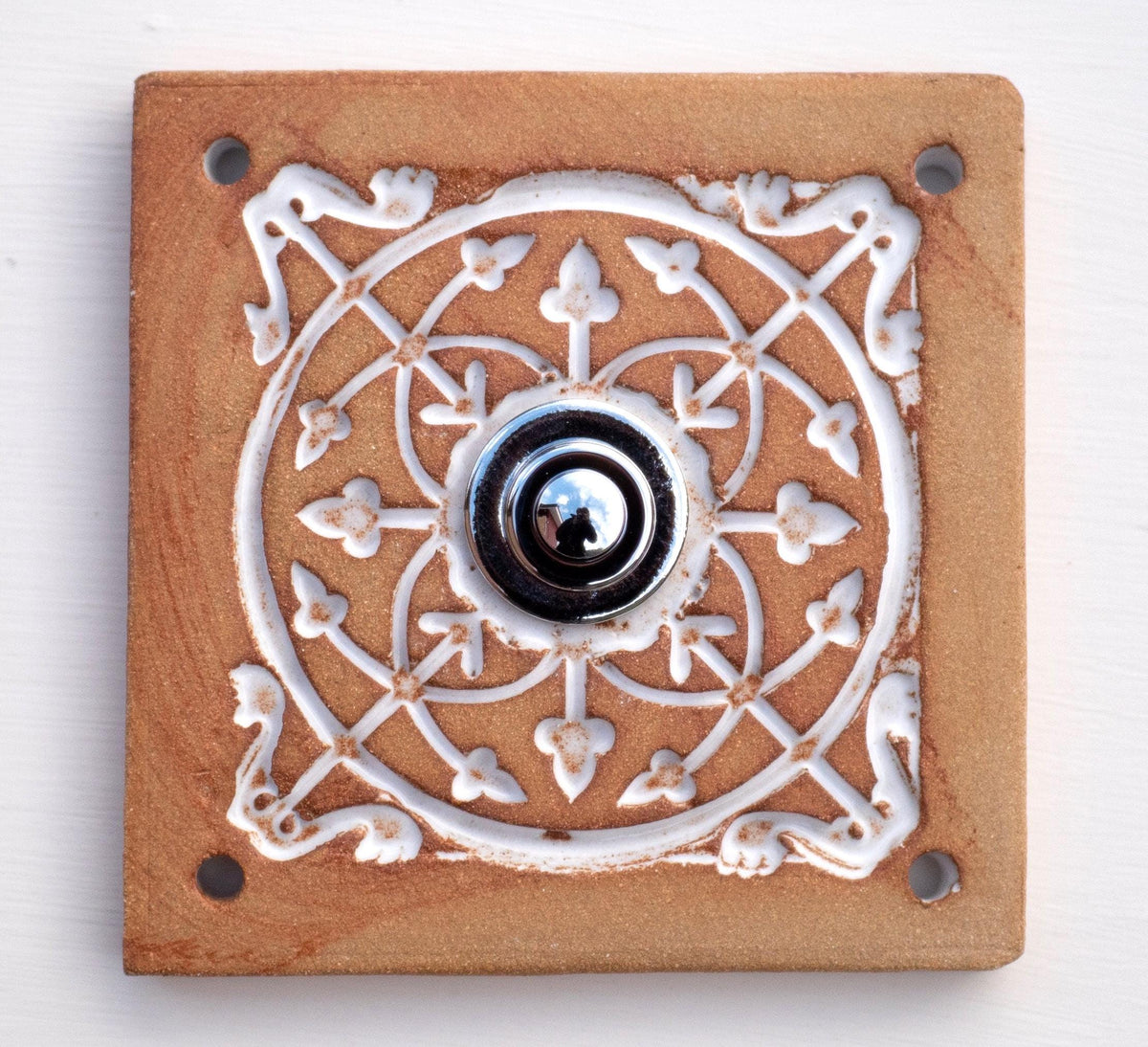 Quadratische Keramikklingel in Goldbraun mit geprägtem weißem Mandala-Muster und silbernem Druckknopf in der Mitte