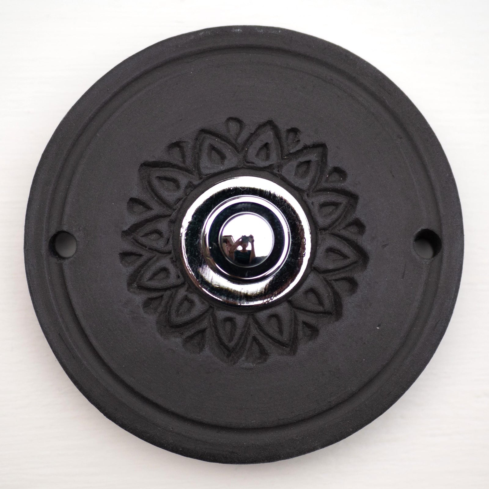 Runde dekorative Klingel mit geprägtem Blumen-Sternmuster auf schwarzer Platte und silbernem Druckknopf in der Mitte.