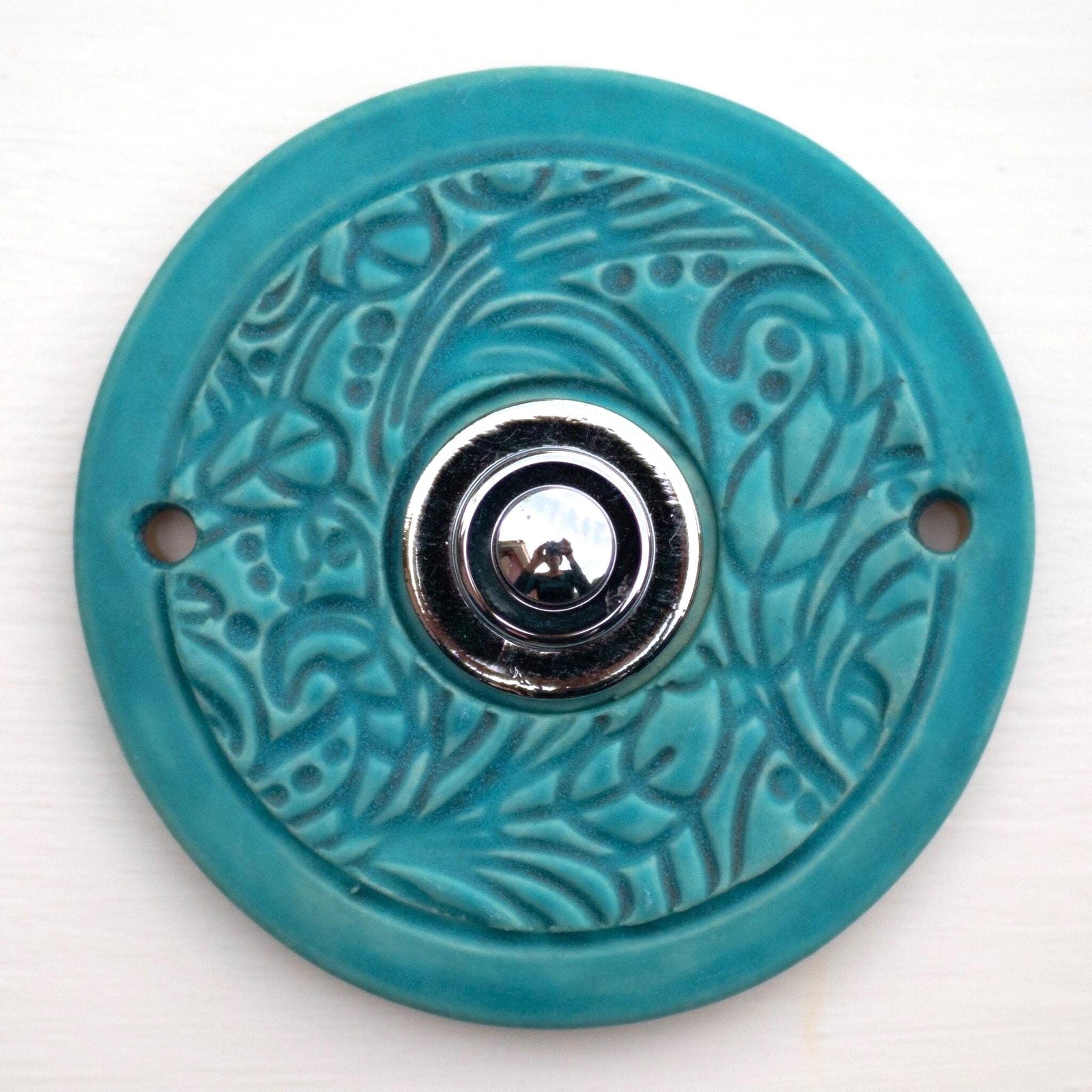 Runde dekorative Klingel mit blauem Ornamentmuster auf grauer Platte und goldenem Druckknopf in der Mitte