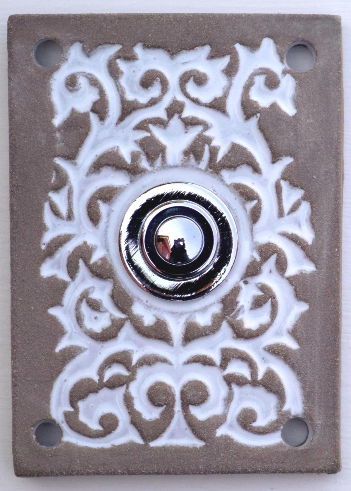 Rechteckige Keramikklingel in Grau-Weiß mit kunstvollem Reliefmuster und silbernem Druckknopf in der Mitte