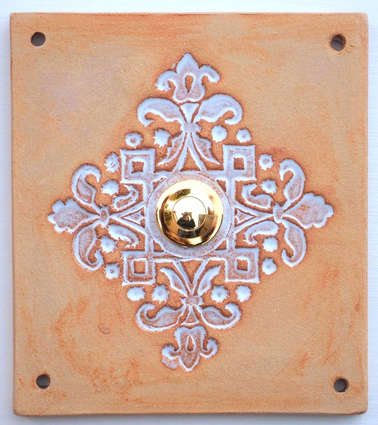 Rechteckige keramische Klingelplatte in Terrakottafarbe mit ornamentaler Prägung in Blumenmotiven und mittigem goldenen Knopf
