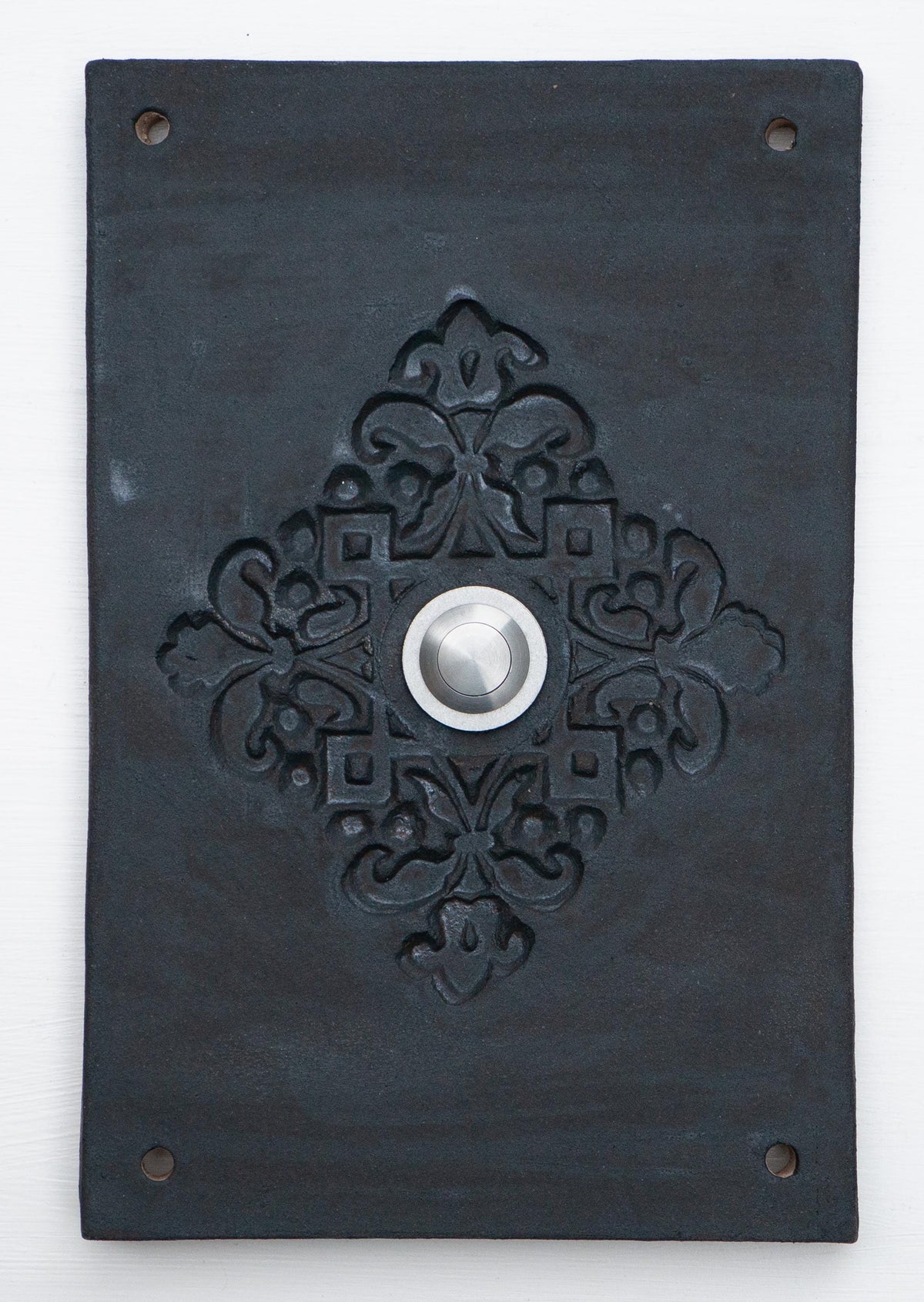 Rein schwarze Keramik-Klingelplatte mit erhabenem ornamentalem Blumenmuster und mittigem Silberknopf.