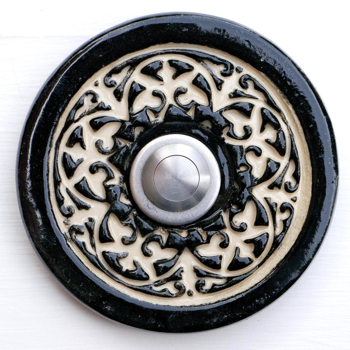Handgefertigte runde Keramiktürklingel in tiefem Schwarz mit kunstvollem cremefarbenem Reliefmuster. Der Edelstahlknopf setzt einen modernen Akzent in diesem eleganten Handwerksdesign.