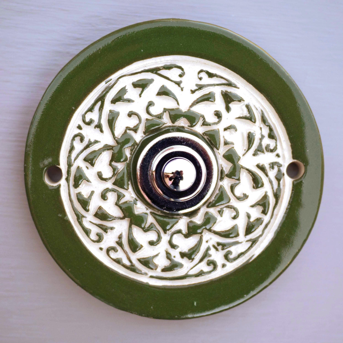 Handgefertigte runde Keramiktürklingel in sattem Grün mit kunstvollem cremefarbenem Reliefmuster. Elegant und langlebig, veredelt mit einem modernen Edelstahlknopf