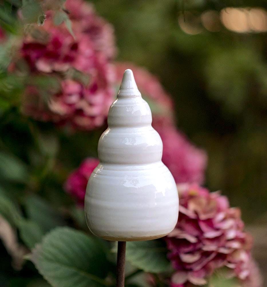 Handgefertigte weiße Keramik-Gartenstele mit gestufter, spitzer Form, dekorativ zwischen blühenden Hortensien platziert.