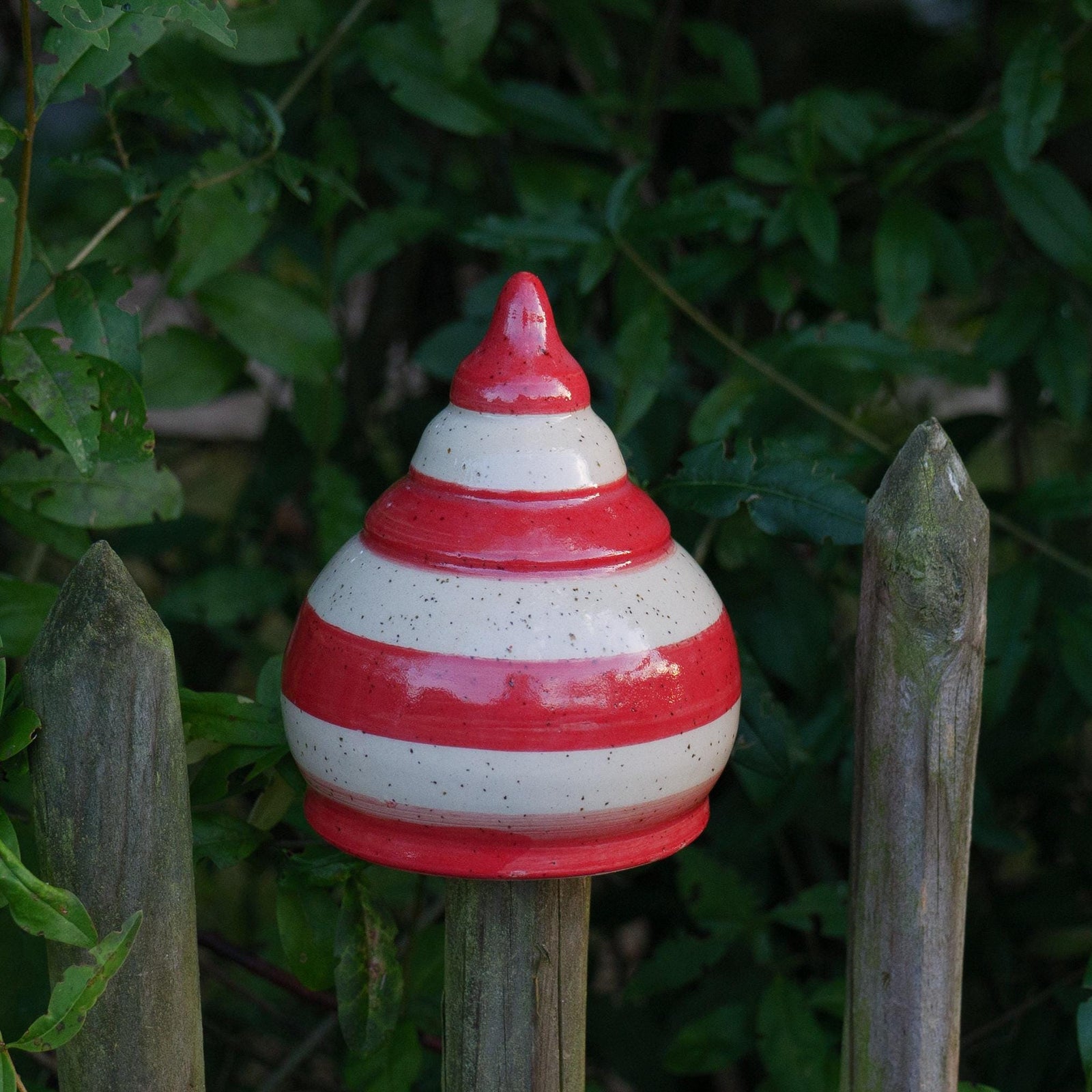 Keramik-Gartenstecker in Tropfenform mit roten und beigen Streifen im Gartenzaun