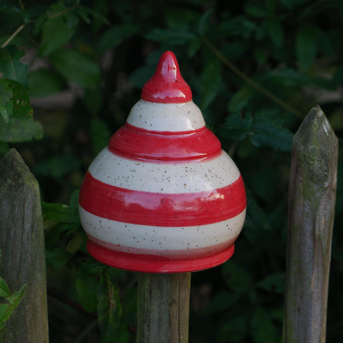 Keramik-Gartenstecker in Tropfenform mit roten und beigen Streifen im Gartenzaun