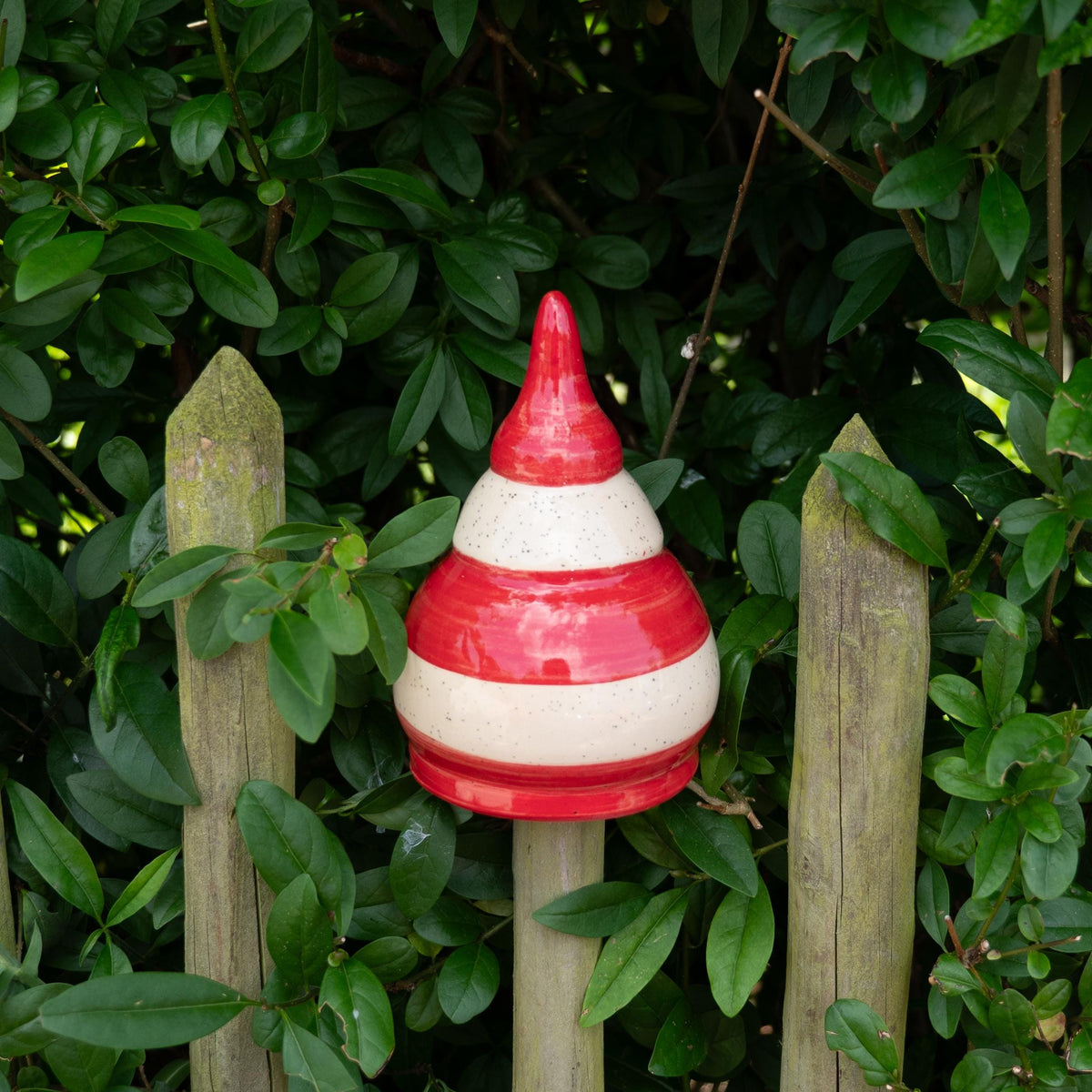 Keramik-Gartenstecker in Tropfenform mit roten und beigen Streifen im Gartenzaun
