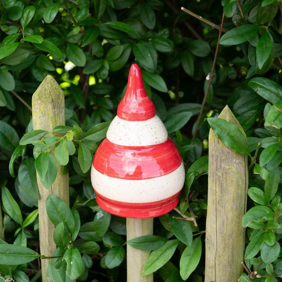 Keramik-Gartenstecker in Tropfenform mit roten und beigen Streifen im Gartenzaun