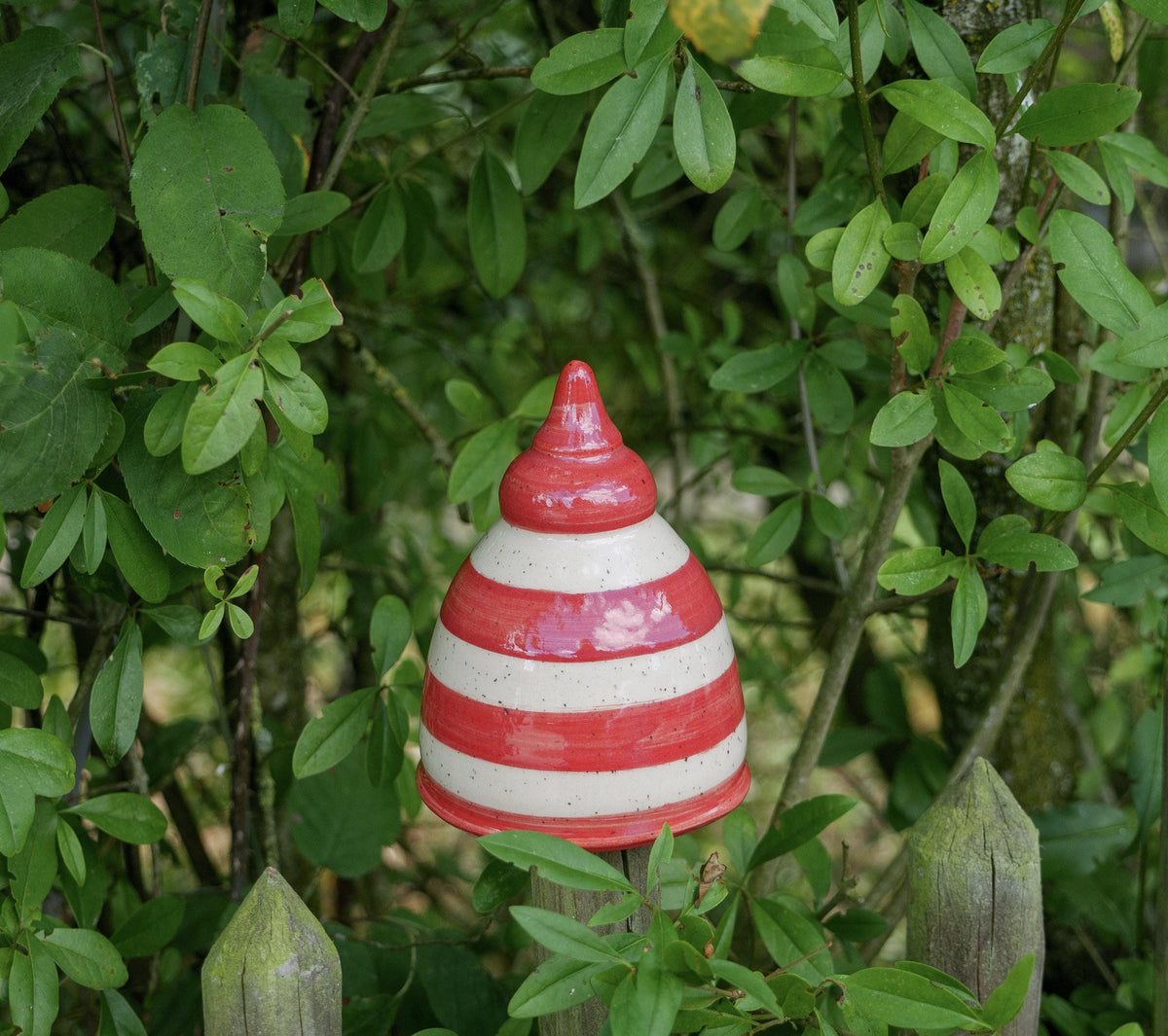 Keramik-Gartenstecker in Tropfenform mit roten und beigen Streifen im Gartenzaun