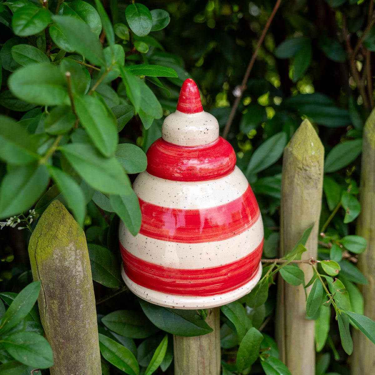 Keramik-Gartenstecker in Tropfenform mit roten und beigen Streifen im Gartenzaun