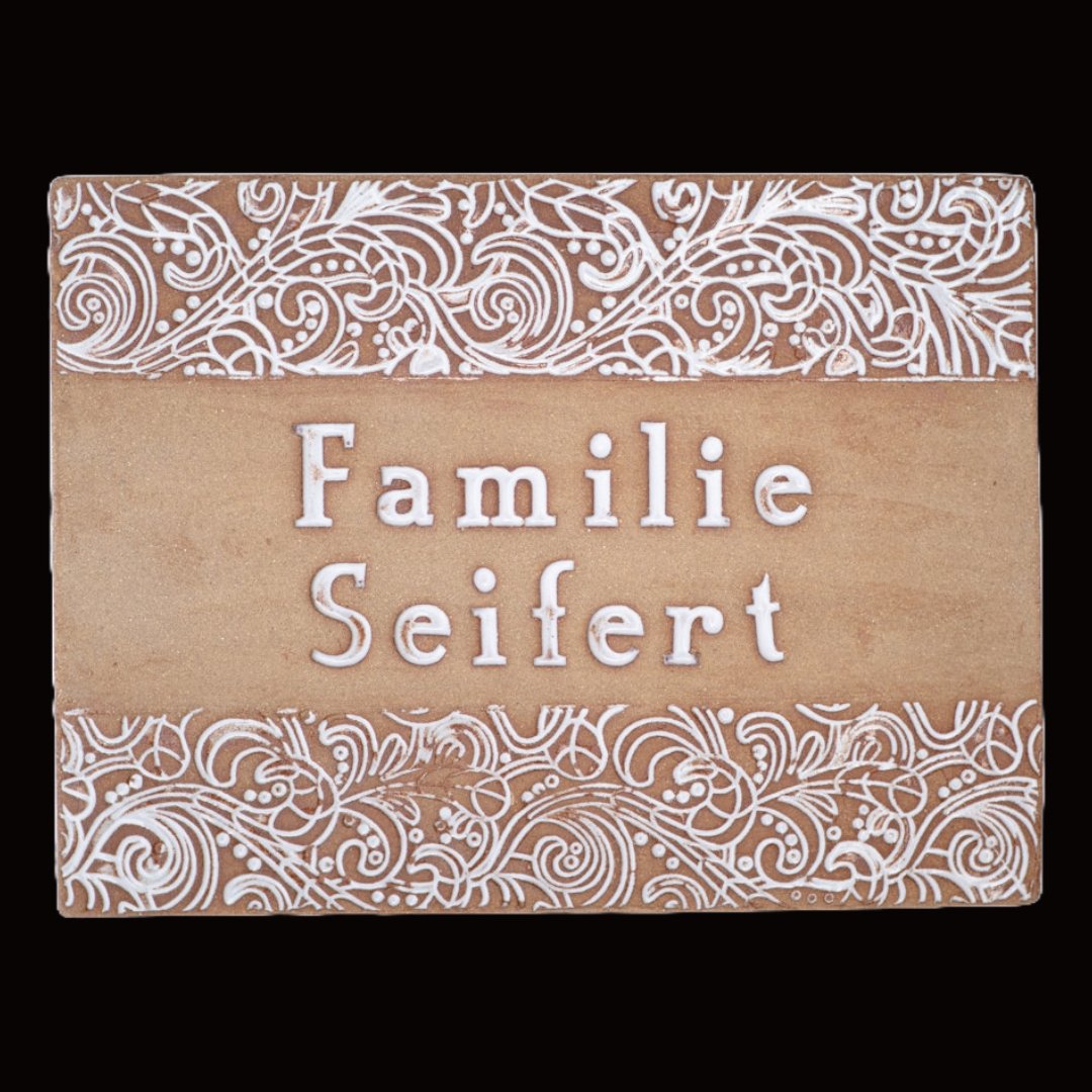 Handgefertigtes Terrakotta-Hausschild mit dekorativen weißen Ornamenten oberhalb und unterhalb des Namens Familie Seifert