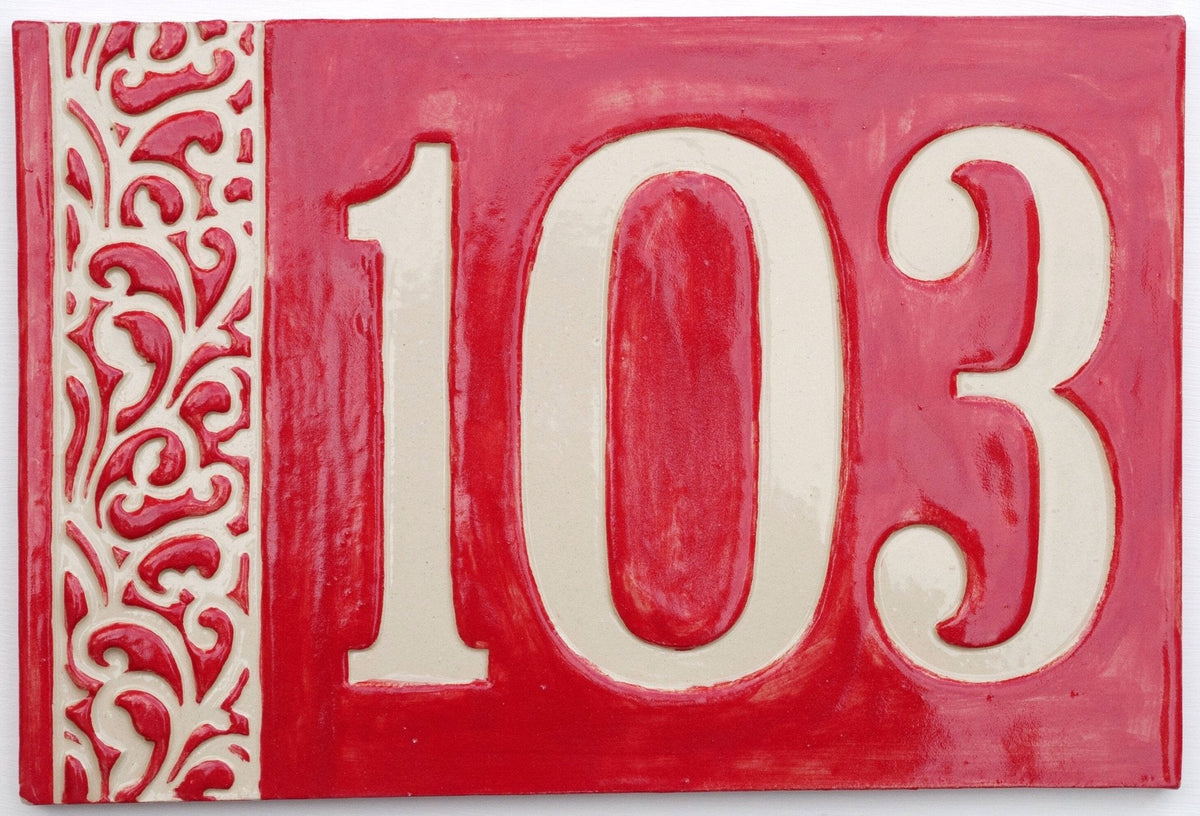 Rechteckiges Keramik-Hausschild mit glänzend rotem Hintergrund, cremefarbenen Reliefziffern 103 und erhabenem cremefarbenem Ziermuster am linken Rand