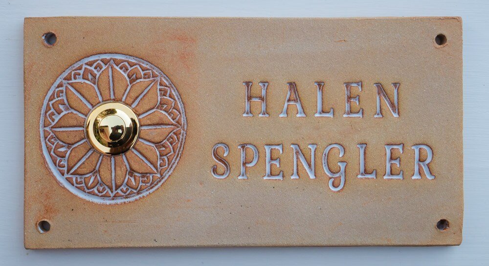 Rechteckiges beiges Keramik-Türschild mit Blumenornament, goldenem Klingelknopf und Namen Halen Spengler