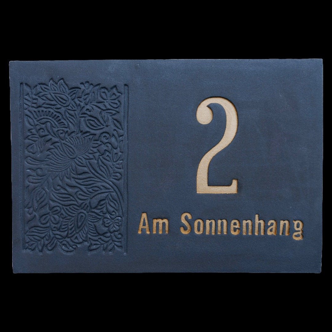 Rechteckiges Keramik-Hausschild in Dunkelblau mit goldfarben eingravierter Zahl 2 und Aufschrift 'Am Sonnenhang', verziert mit floraler Gravur auf der linken Seite