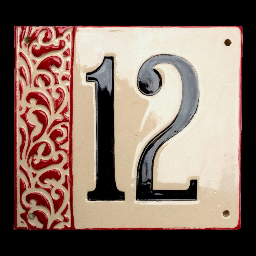 Quadratisches Keramik-Hausschild mit cremefarbenem Hintergrund, glänzenden schwarzen Reliefziffern 12 und erhabenem roten Ziermuster am linken Rand