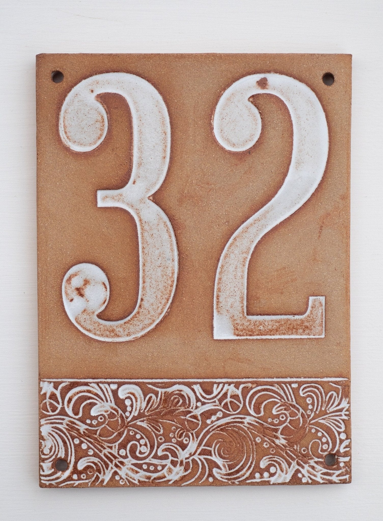 Beiges Keramik-Hausschild mit erhabenen weißen Ziffern 32 und dekorativem floralem Muster am unteren Rand