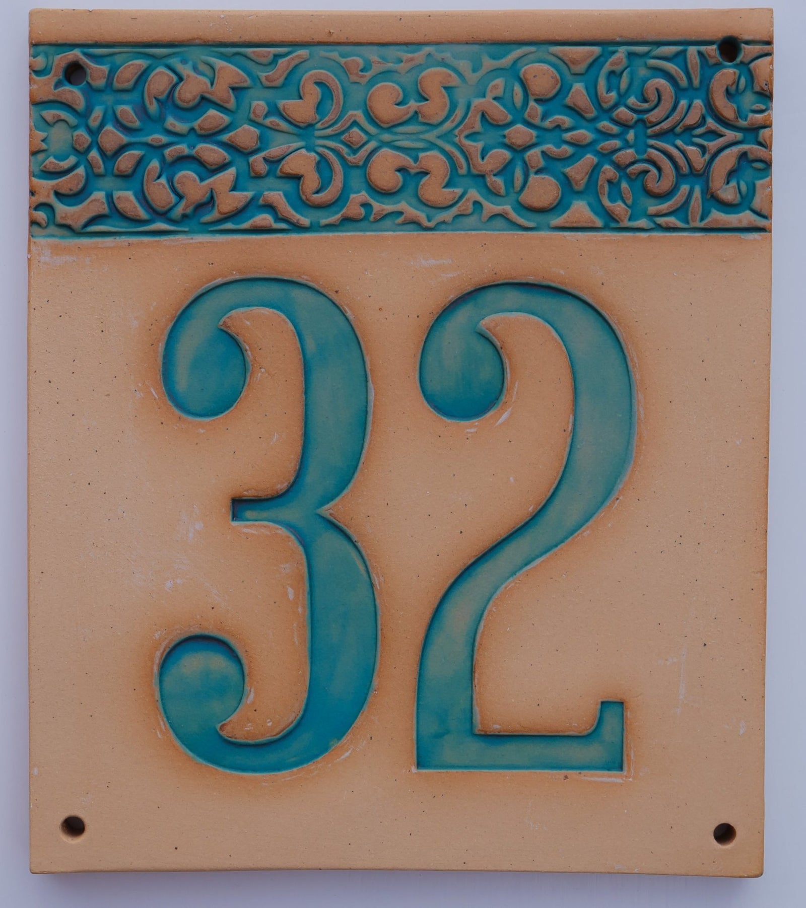 Rechteckiges Keramik-Hausschild mit beigem Hintergrund, türkisfarbenen Reliefziffern 32 und ornamentalem türkisfarbenem Rand auf der linken Seite