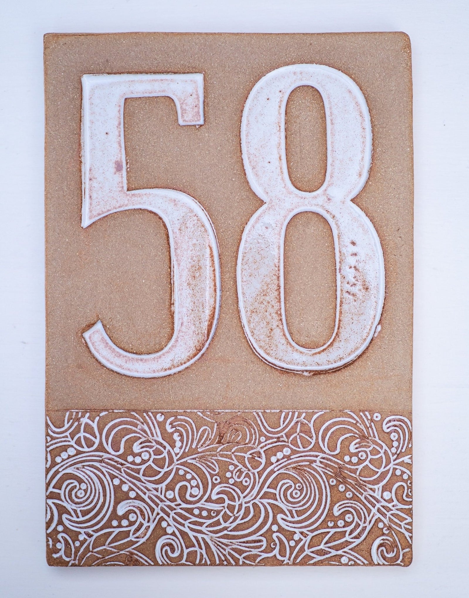 Beiges Keramik-Hausschild mit erhabenen weißen Ziffern 58 und dekorativem floralem Muster am unteren Rand