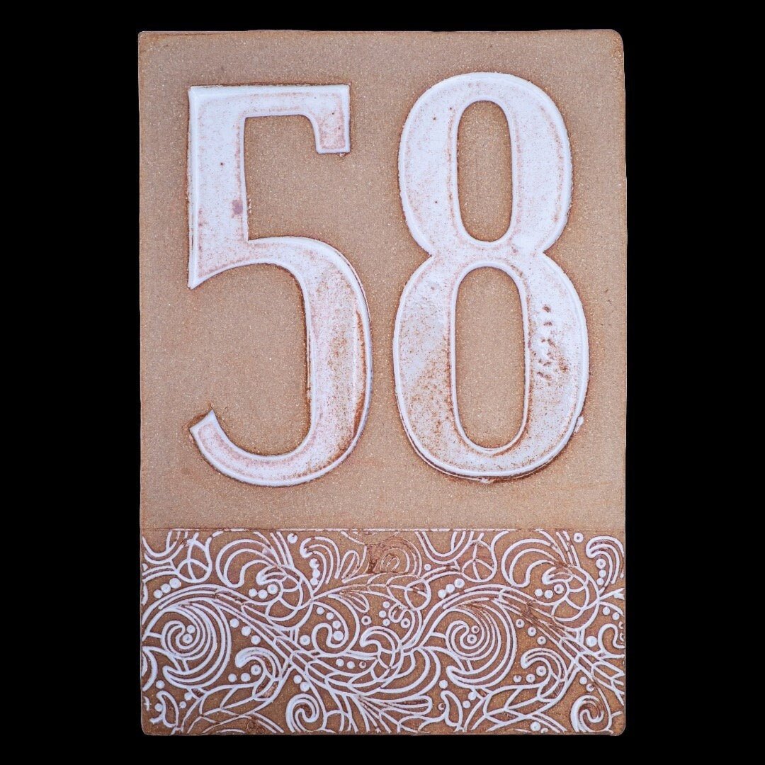 Beiges Keramik-Hausschild mit erhabenen weißen Ziffern 58 und dekorativem floralem Muster am unteren Rand