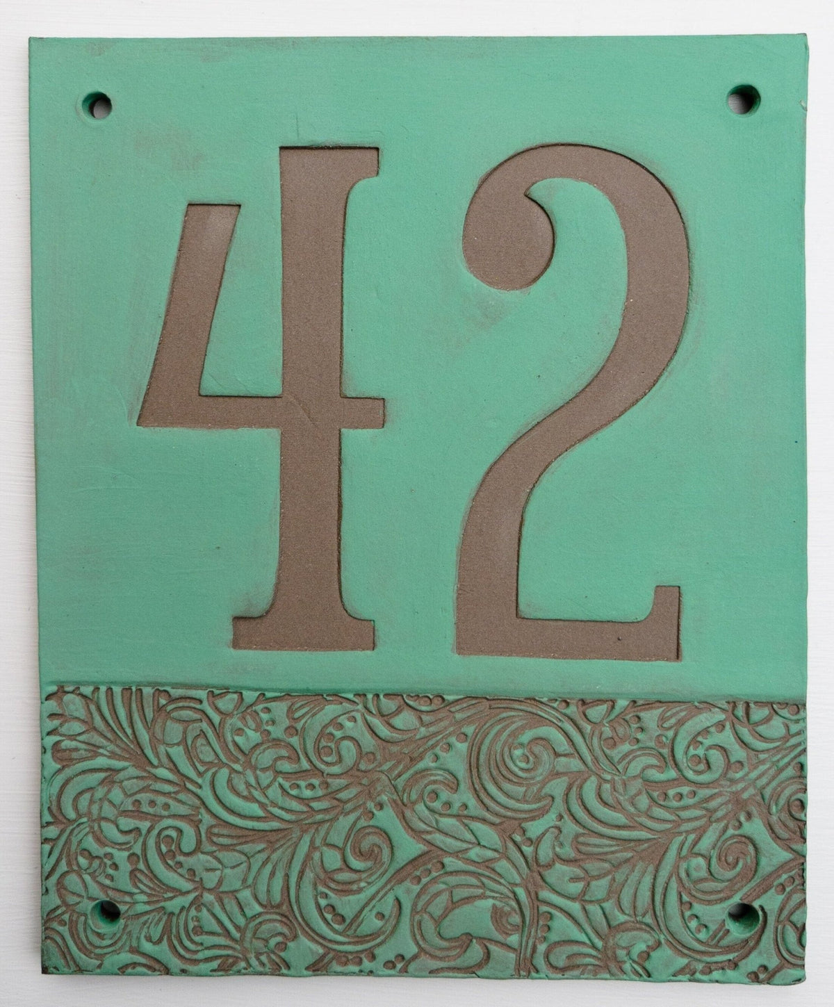 Rechteckiges Keramik-Hausschild mit mattem grünem Hintergrund, eingravierten tonfarbenen Ziffern 42 und dekorativem Blumenmuster im unteren Bereich