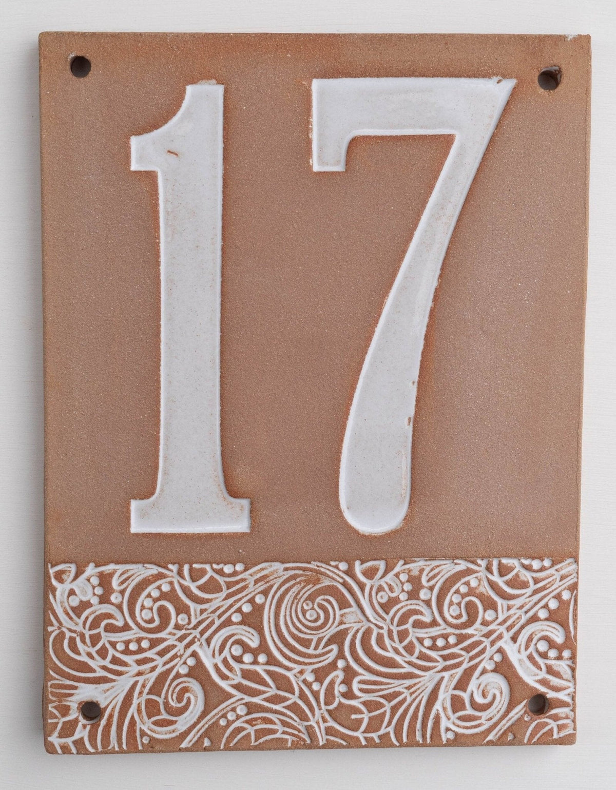Beiges Keramik-Hausschild mit erhabenen weißen Ziffern 17 und dekorativem floralem Muster am unteren Rand