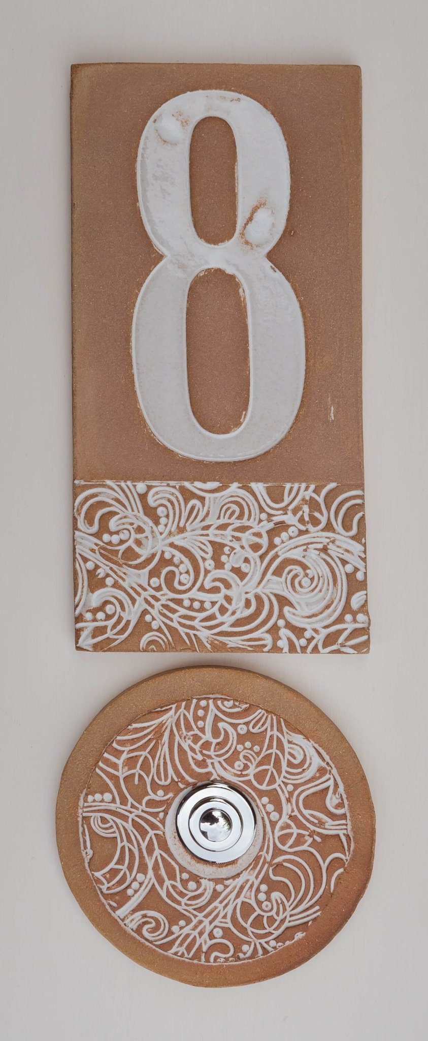 Beiges Keramik-Hausschild mit erhabenen weißen Ziffern 8 und dekorativem floralem Muster am unteren Rand