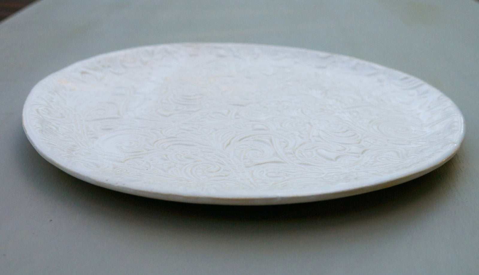 Runder weißer Keramikteller mit geprägtem Blumen- und Wirbelmuster.