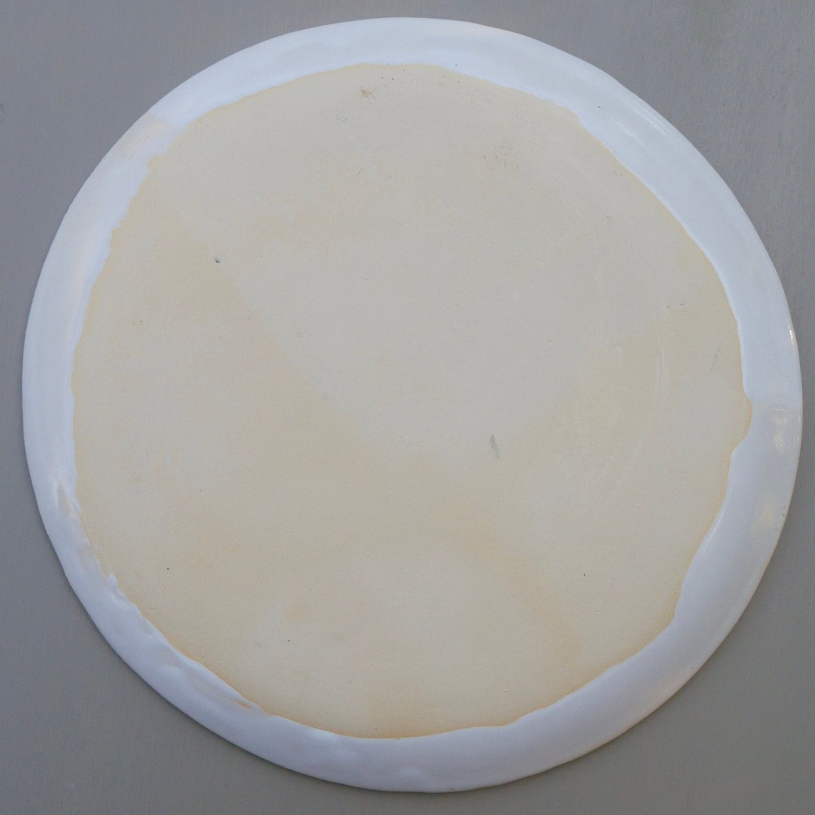 Runder weißer Keramikteller mit geprägtem Blumen- und Wirbelmuster.