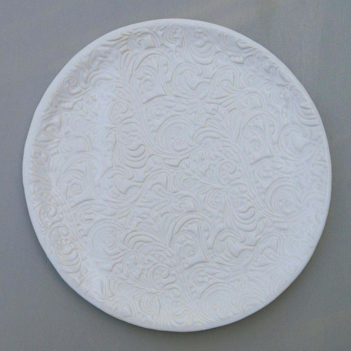 Runder weißer Keramikteller mit geprägtem Blumen- und Wirbelmuster.