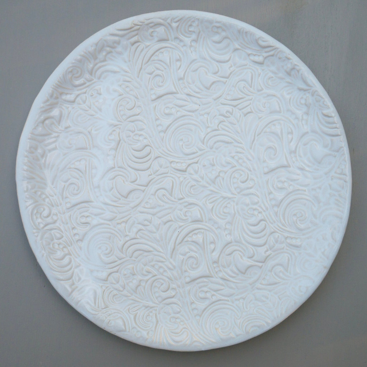 Runder weißer Keramikteller mit geprägtem Blumen- und Wirbelmuster.