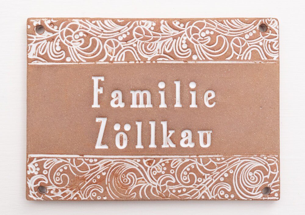 Handgefertigtes Terrakotta-Hausschild mit dekorativen weißen Ornamenten oberhalb und unterhalb des Namens Familie Seifert