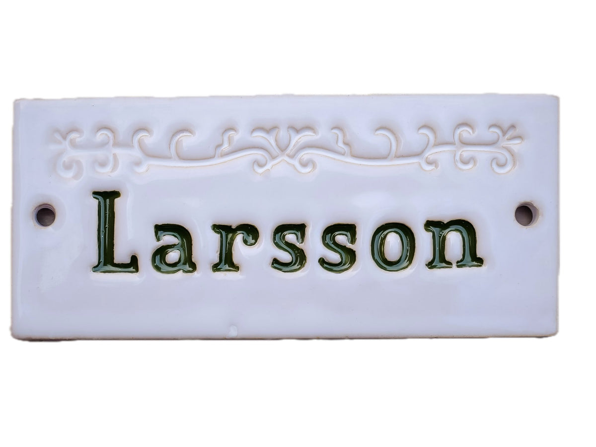 Handgefertigtes weißes Namensschild mit roter Inschrift Larsson und Zierornament