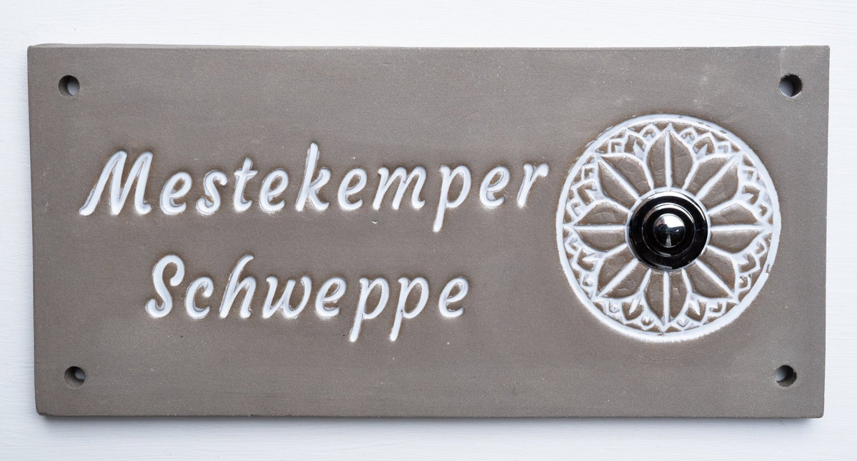 Rechteckiges graues Keramik-Türschild mit weißem Blumenornament, schwarzem Klingelknopf und Namen Mestekemper Schweppe