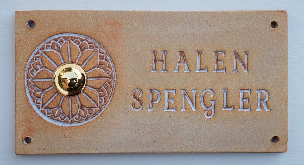 Rechteckiges beiges Keramik-Türschild mit Blumenornament, goldenem Klingelknopf und Namen Halen Spengler
